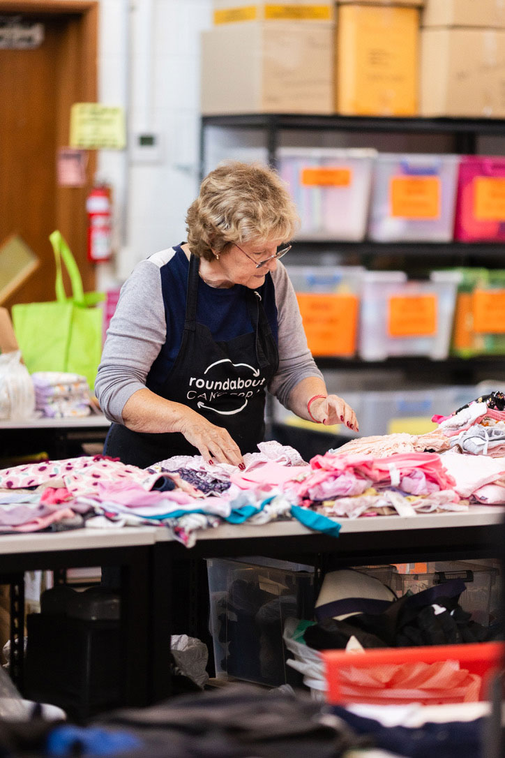 Roundabout Canberra volunteer sorting donated baby and children's clothes by size and type on a large table in the donation centre.