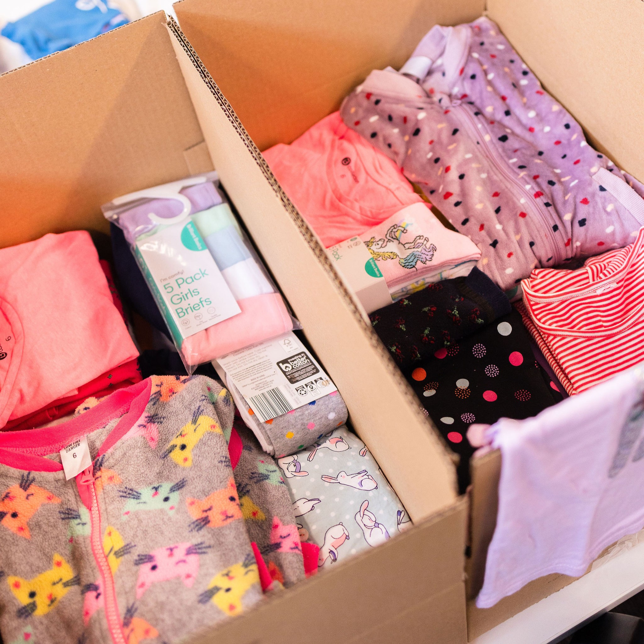 Two cardboard boxes filled with neatly folded girls' clothing and underwear, including pyjamas, briefs, and tops, ready for distribution by Roundabout Canberra.